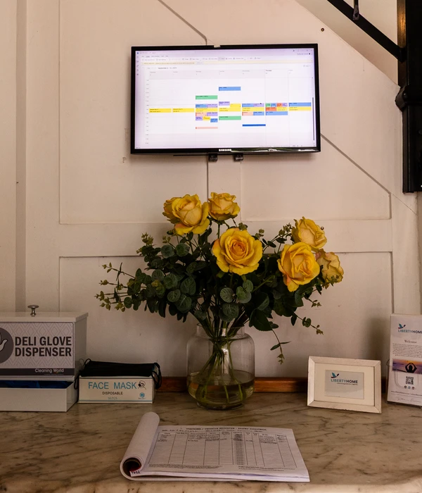Een marmeren receptiebalie met een vaas gele rozen, een bezoekersregister en een digitaal programmaoverzicht aan de muur.