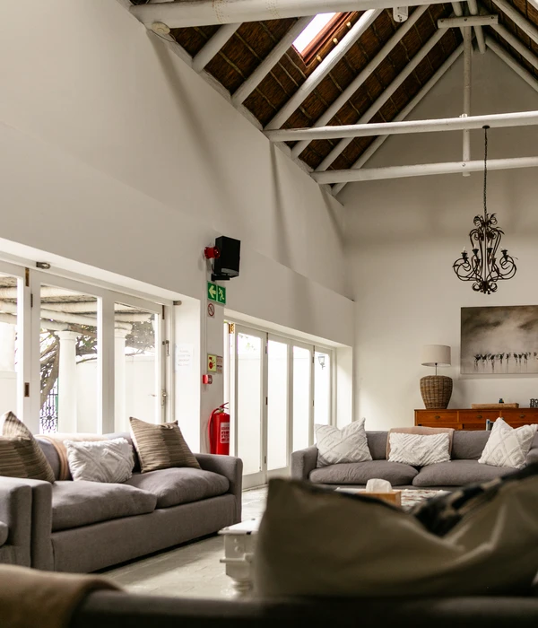 Lichte gemeenschappelijke lounge met grijze banken, een fraai bewerkte salontafel, openslaande glazen deuren naar een patio en een brandblusser aan de muur.