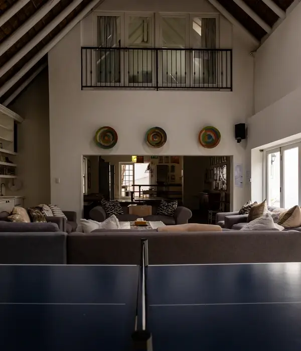 Ruime gemeenschappelijke lounge met grijze banken, een pingpongtafel op de voorgrond en een mezzaninebalkon onder een hoog plafond.