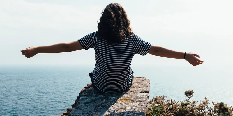 woman sitting on a cliff overlooking the sea